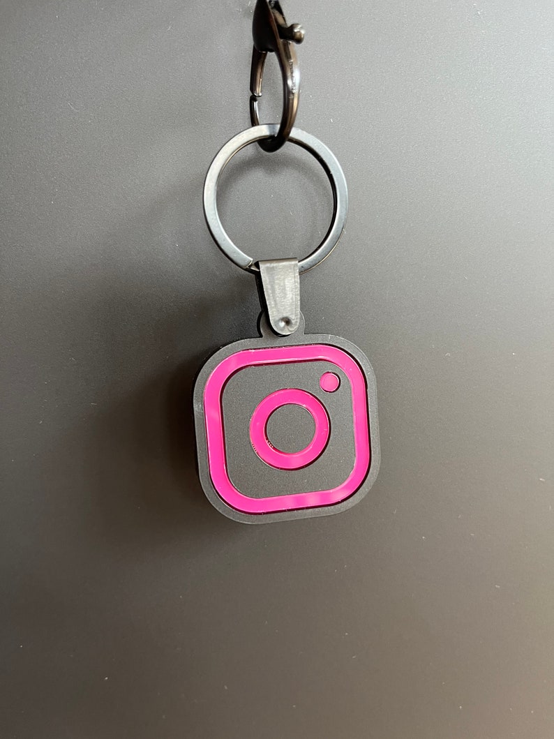 May include: A black and pink Instagram logo keychain with a silver metal ring.