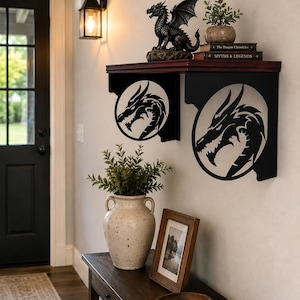 May include: A wall-mounted shelf featuring two black metal brackets with circular cutouts displaying a dragon head silhouette. The shelf has a dark wood top surface. The brackets are mounted to a light-colored wall, providing a sturdy platform for decor.