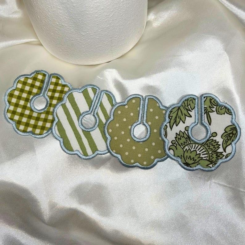 May include: Four decorative bottle collar covers with scalloped edges and a light blue trim. Each collar features a different pattern: green gingham, green stripes, green polka dots, and a green floral design.