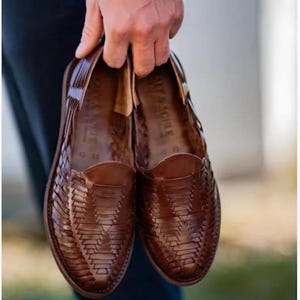 May include: A pair of brown leather huarache shoes featuring a woven lattice pattern across the upper and a closed toe design. The interior of the shoes displays the brand name Salt & Sohle stamped on the leather footbed with a visible size 12.