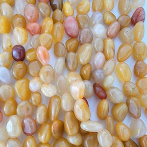 May include: A collection of polished, oval-shaped gemstones in shades of yellow, orange, and peach. The stones vary in size and translucence, with some appearing more opaque and others nearly transparent. The arrangement is scattered, creating a natural, organic aesthetic.