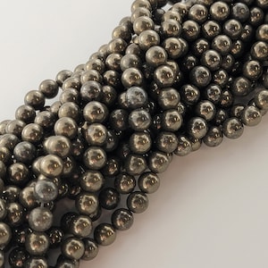 May include: A close-up of a pile of round, metallic gold pyrite beads. The beads are smooth and have a slightly rough texture.