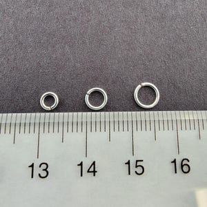May include: Three silver jump rings of different sizes, measured against a ruler with markings from 13 to 16.