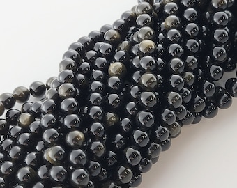 May include: A close-up of a strand of black and gold gemstone beads. The beads are round and have a smooth, polished finish.