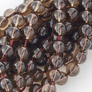 May include: A strand of brown smoky quartz beads with a red thread running through the center. The beads are round and have a translucent appearance.