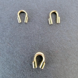 May include: Three gold-colored metal U-shaped clasps. Each clasp has a rounded top and two parallel, open-ended legs. The clasps are arranged on a dark gray surface.