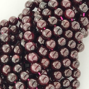 May include: A strand of dark red gemstone beads. The beads are round and have a smooth, polished finish.