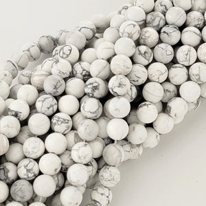 May include: A strand of white and gray round beads made of natural Howlite. The beads are smooth and have a marbled pattern.