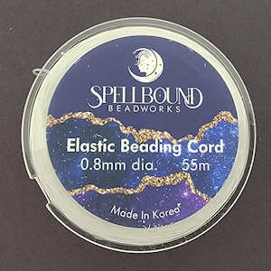May include: A spool of clear elastic beading cord. The label reads "Spellbound Beadworks" with the text "Elastic Beading Cord 0.8mm dia. 55m". The label has a dark blue background with a starry design and gold accents. Made in Korea.