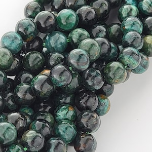 May include: A strand of dark green and black round gemstone beads. The beads have a mottled, speckled appearance.
