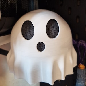 Può includere: Altoparlante bianco a forma di fantasma con griglie per altoparlanti in rete nera per occhi e bocca.