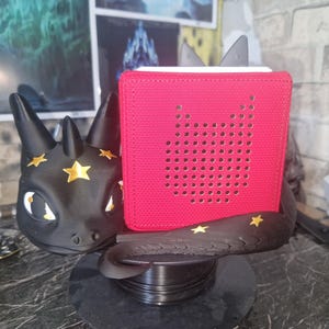 May include: A black dragon-themed speaker stand with gold star details, supporting a red speaker. The speaker features a perforated design. The stand sits on a black base, creating a unique decorative piece.