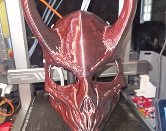 May include: A 3D printed red mask with horns. The mask has a detailed skull design and a textured surface.