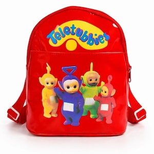 May include: A red backpack featuring the Teletubbies characters. The backpack has a front pocket and adjustable straps. The Teletubbies logo is at the top. The backpack is approximately 12 inches tall and 10 inches wide.