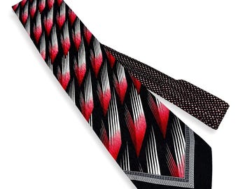 May include: A necktie with a striking geometric pattern. The tie features a repeating design of red and white shapes against a black background. The tip of the tie has a black border with a gray and white patterned trim.