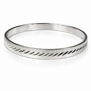 May include: A silver bangle bracelet with a repeating diagonal cut pattern around the band. The bracelet is circular and has a smooth, polished finish. The design is simple and elegant.