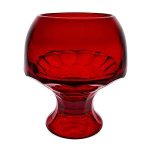 Pode incluir: Um cálice de vidro vermelho rubi com uma taça arredondada e uma base de pedestal. A taça tem um design decorativo com vieiras. O vidro é transparente, permitindo a passagem da luz. O cálice é provavelmente usado para servir bebidas.