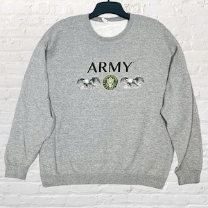 May include: A heather gray sweatshirt with the word "ARMY" printed across the chest. Below the word "ARMY" is a graphic of two eagles flanking a circular emblem. The sweatshirt is hanging on a black hanger.