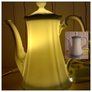 Könnte beinhalten: Eine weiße Porzellan-Teekanne mit blauem Rand und gelbem Schein. Die Teekanne wird von innen beleuchtet und erzeugt eine warme und einladende Atmosphäre.