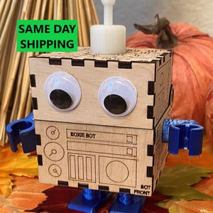 May include: A wooden robot toy with googly eyes, blue arms and legs, and the text "Boxie Bot" and "Bot Front" on the front.