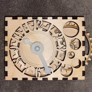 May include: A wooden puzzle box with a clock face design. The clock face has cut-out numbers and a white plastic clock hand. The box has a gear on the side and several circular cut-outs. The wood is light brown.