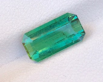 May include: A green emerald gemstone cut into a rectangular shape with a faceted finish.