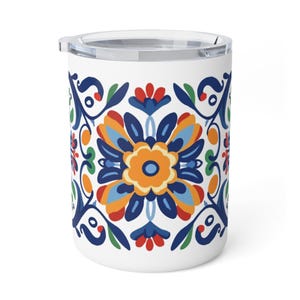 Op de afbeelding: Witte reismok met een kleurrijk bloemmotief. Het patroon heeft een centrale oranje bloem omringd door blauwe, rode en groene accenten. De mok heeft een doorzichtig deksel en is ontworpen voor warme of koude dranken.