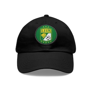 Puede incluir: Gorra de béisbol negra con un parche bordado verde y amarillo que presenta un león y un balón de fútbol con la palabra "LEON" en letras amarillas.