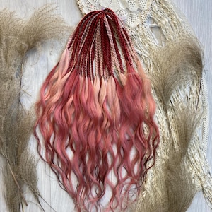 Könnte beinhalten: Ein Set aus roten, rosa- und hellblonden Kunsthaar-Dreadlocks mit welligen Enden. Die Dreadlocks sind auf einer hellen Holzoberfläche mit dekorativen Elementen wie getrockneten Gräsern und einer weißen Spitzendecke angeordnet.