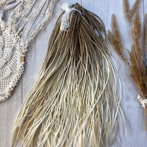 May include: Ombre hair extensions, fading from brown to blonde, tied with a white lace ribbon. A white lace dreamcatcher and dried wheat are also visible in the image.