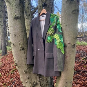 May include: A brown blazer with a double-breasted closure and a green embroidered design on the right sleeve.