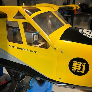 May include: Yellow and black model airplane with a clear cockpit and the text "Pilot: Brooks Gant" and "District 51 RC Lab" on the side.