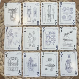 May include: A deck of playing cards with a unique design. Each card features a blueprint-style engineering drawing in blue and white. The cards display various mechanical designs, including gears, engines, and other machine components. The suits are represented by traditional symbols, and the card values are visible.