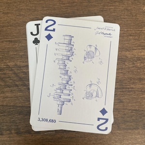 Two playing cards are displayed. The first card is a Jack of Clubs. The second card is a Two of Diamonds, featuring a blue engineering drawing of an engine component. The card also has the number '2' in the bottom right corner and the text '3,308,680' at the bottom. The top right corner has the text 'Everett & Sherrick BY J.L. Carpenter ATTORNEY'.