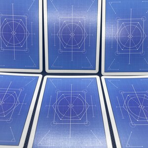 May include: A collection of playing cards with a blueprint design. Each card features a blue background with white geometric shapes, including circles, lines, and angles. The cards have white borders and a clean, modern aesthetic.