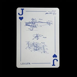 May include: A playing card featuring the Jack of Hearts. The card has a white background with blue ink illustrations of an airplane blueprint. The top right corner has a signature and text. The bottom left corner has the number 1,316,278.