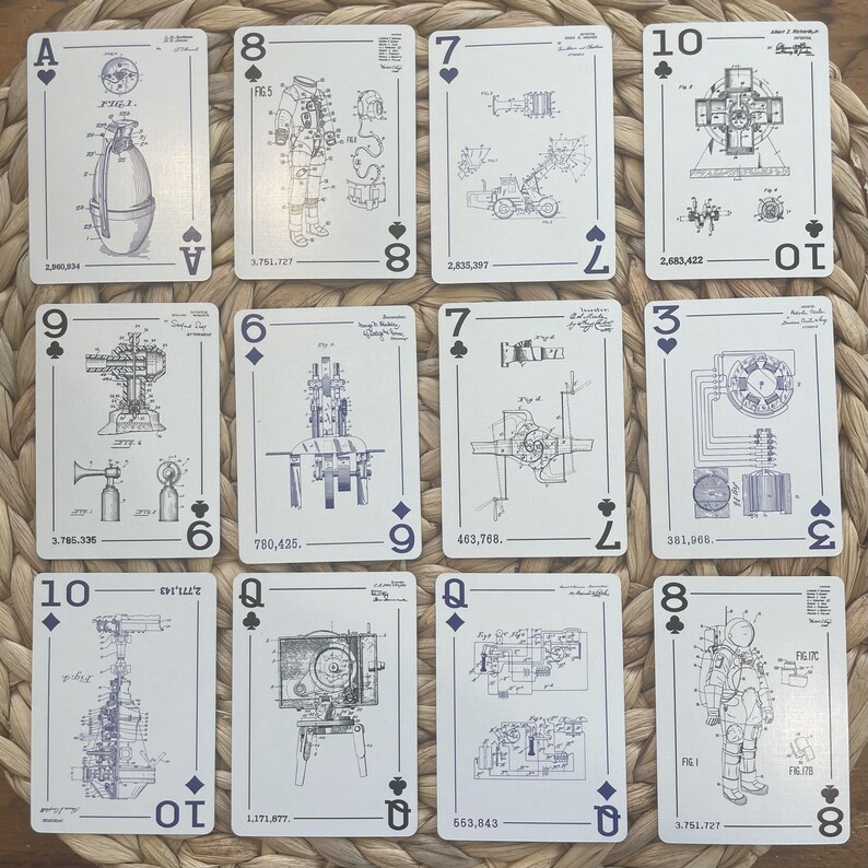 Playing cards with patent illustrations. The cards feature various inventions, including a space suit, and machinery. Each card displays a suit symbol and number or face value. The designs are in black and white, with text indicating patent numbers and figures. The cards are arranged on a woven surface.