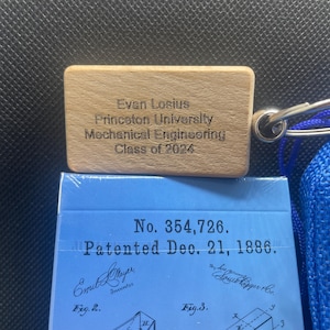 A deck of cards with a wooden keychain sitting above it that reads "Evan Losious, Princeton University, Mechanical Engineering, Class of 2024"