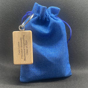 A blue drawstring baggy with a wooden keychain attached that reads "Evan Losious, Princeton University, Mechanical Engineering, Class of 2024"