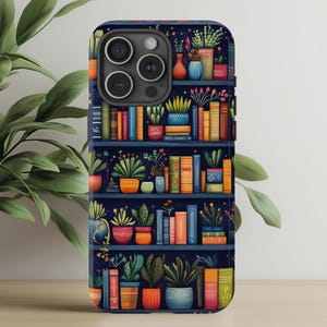 Op de afbeelding: Telefoonhoesje met een grillige illustratie van een boekenplank vol kleurrijke boeken en potplanten. Het ontwerp heeft een donkerblauwe achtergrond met levendige oranje, groene en blauwe accenten, wat een gezellig, literair thema creëert.