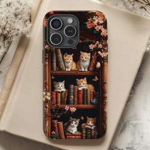 May include: A phone case with a design of kittens sitting on a bookshelf with books. The kittens are all different colors and have different expressions. The bookshelf is made of wood and has a floral design. The phone case is black and has a camera cutout.