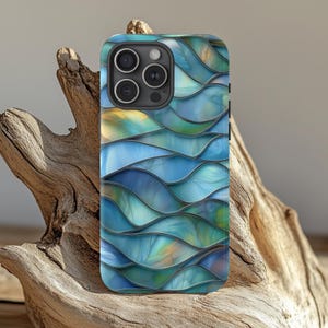 Puede incluir: Funda de teléfono inteligente con un diseño de ondas en tonos azules, turquesas y amarillos. La funda tiene un acabado brillante y un módulo de cámara negro. La funda está sobre un trozo de madera flotante.