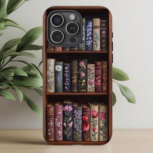 May include: A phone case with a bookshelf design featuring a variety of books with floral illustrations. The case has a brown wooden frame and a clear back panel to show the phone.
