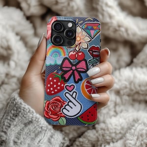 May include: A colourful phone case featuring a variety of embroidered patches, including a rainbow, a heart, a strawberry, a cherry, a bow, a diamond, a flower, a watermelon, and a citrus fruit. The case is designed for an iPhone.