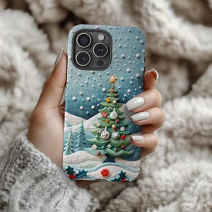 May include: A blue phone case featuring a 3D Christmas tree design with a star on top, ornaments, and a snowy landscape. The case has a textured surface and is decorated with holly and berries. The phone case is held in a hand.