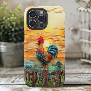 May include: A phone case featuring a colorful rooster standing on a wooden fence against a sunset backdrop. The rooster has red, blue, and yellow feathers. The background depicts a rural landscape with rolling hills and a bright sun.