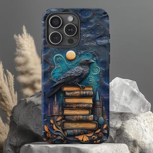 Puede incluir: Un cuervo negro posado sobre una pila de libros antiguos con un fondo de noche estrellada. La funda del teléfono está hecha de un material texturizado azul oscuro con un diseño de luna y estrellas.