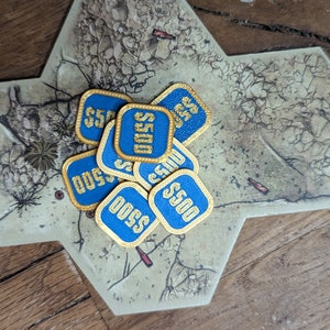 May include: A close-up of a game board with a pile of blue and gold tokens. The tokens have the number "5000" printed on them.