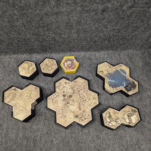May include: A set of six hexagonal game tiles featuring various designs, including a desert scene, a lake, and a rocky area. The tiles are made from cardboard and have a black border. There is also a small yellow hexagonal tile with a skull and crossbones design.