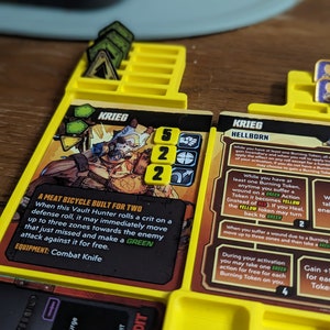 Puede incluir: Una carta de juego de mesa amarilla y negra con un personaje llamado Krieg, con un fondo verde y un texto que dice "A Meat Bicycle Built for Two". La carta tiene un token de acción verde, amarillo y rojo, y un token de dados verde, amarillo y rojo. La carta también tiene un token de acción verde, amarillo y rojo.